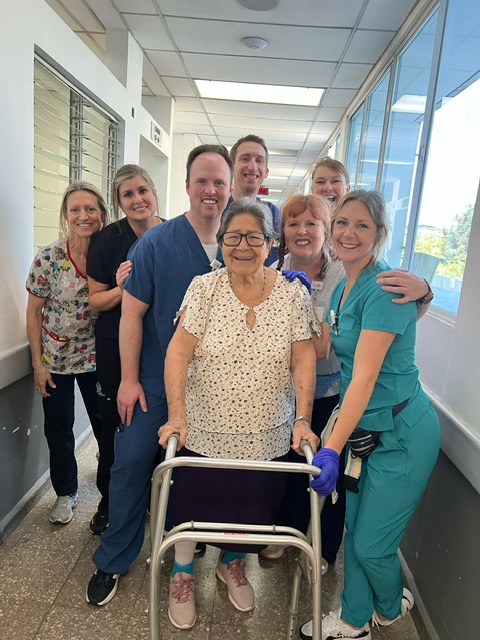 A patient standing with her walker, surrounded by smiling volunteer nurses