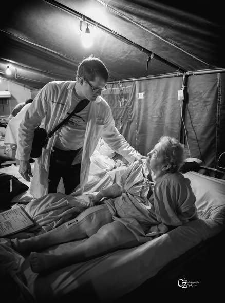 Dr. Daines comforting a patient recovering in a field tent, holding her hand