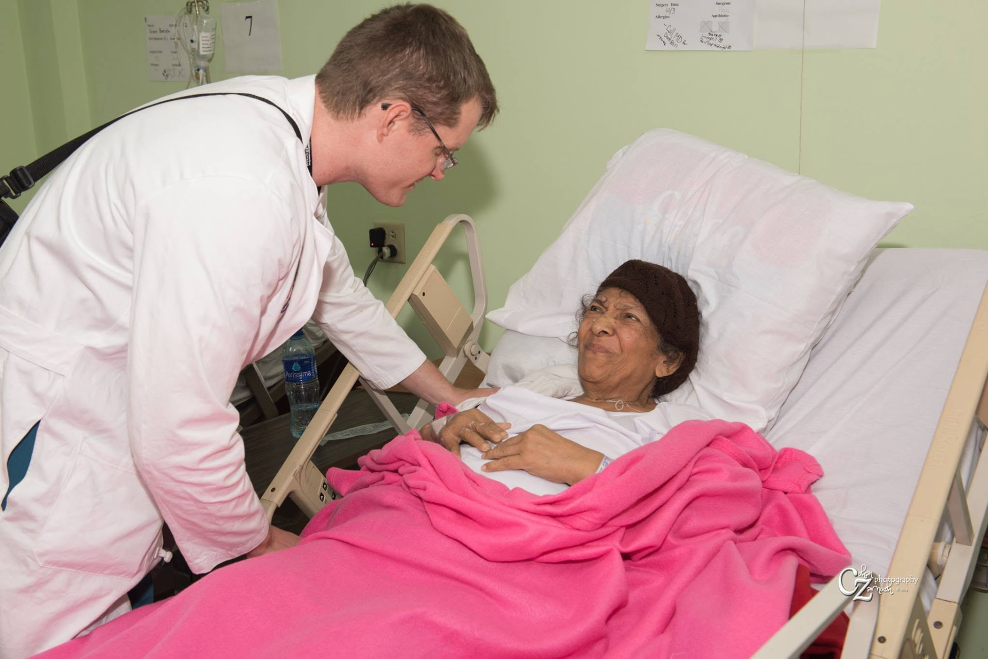 Dr. Daines checking on a smiling patient resting in her hospital bed after surgery