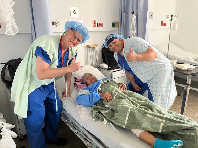 Surgeons giving a thumbs up beside a recovering patient